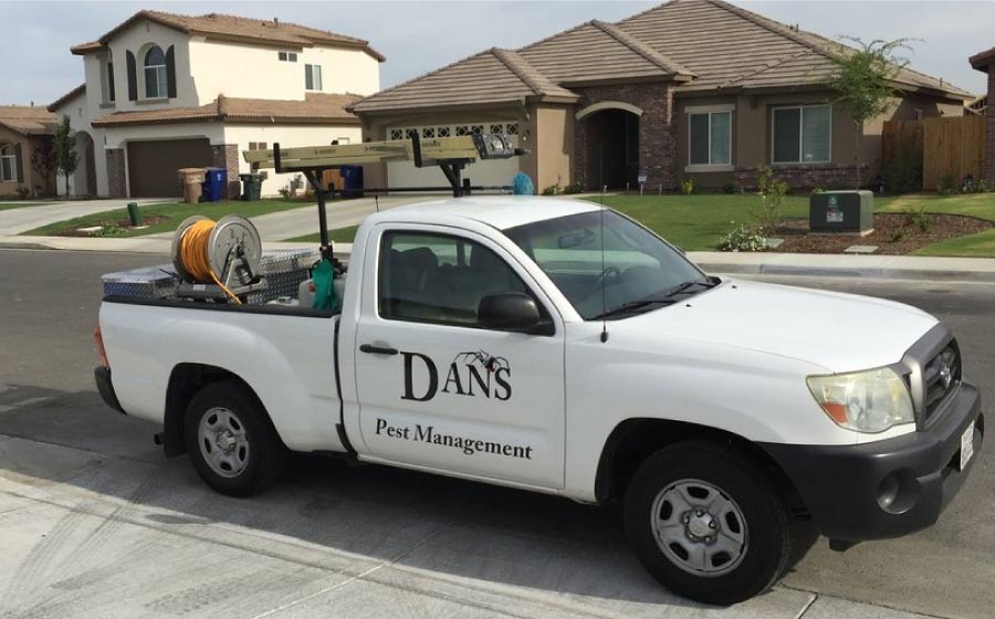 Dan's Pest Management white service truck with professional spray equipment parked in front of a residential home in Kern County, ready for pest and tick control service.